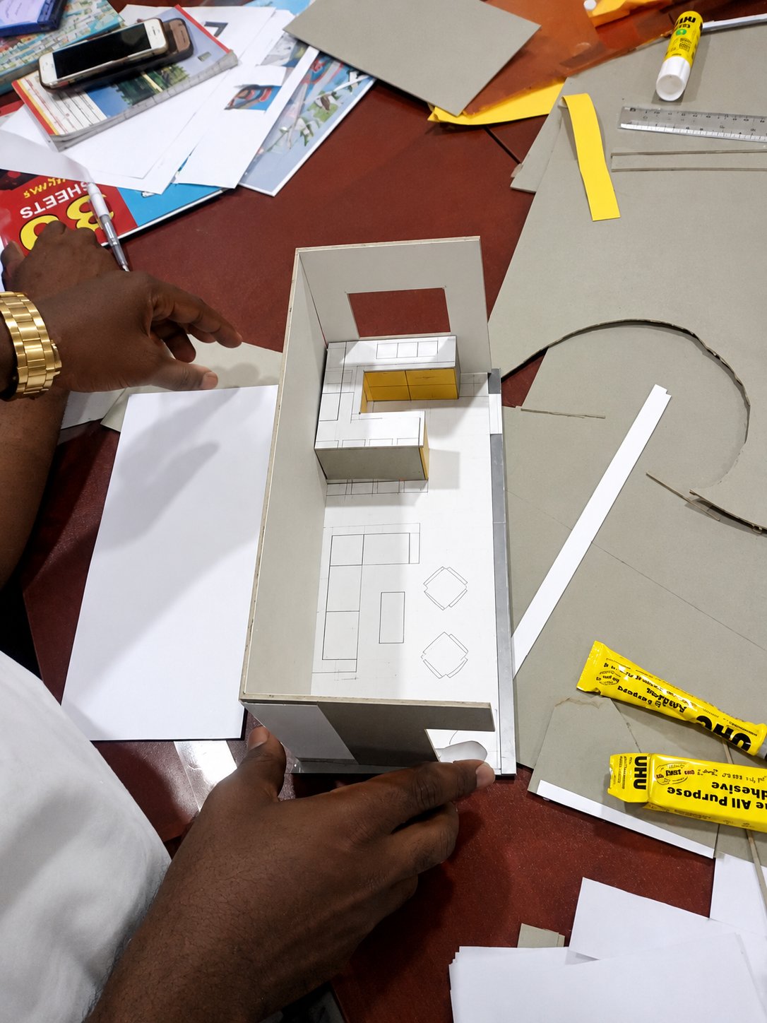 A student assembling a scale card model of a room on the studio table