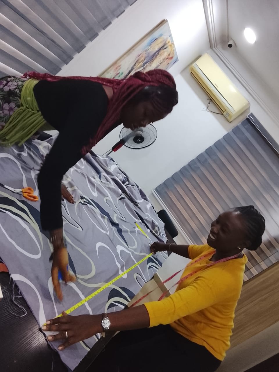Two students measuring patterned curtain fabric across a work table